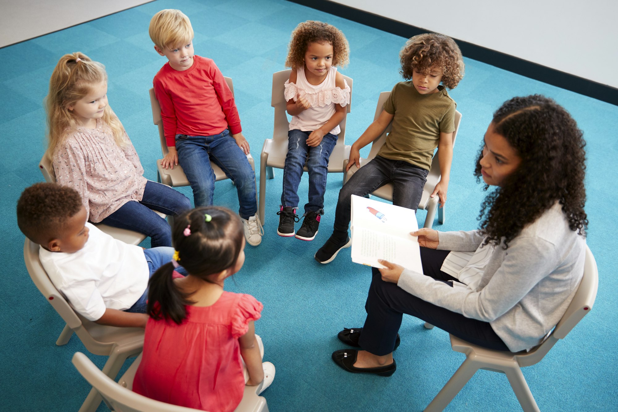 Young female school teacher reading a book to infant school children